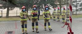 Na zdjęciu widoczni są 3 strażacy w ubraniu bojowym , niosący flagę RP w celu jej podniesienia. 