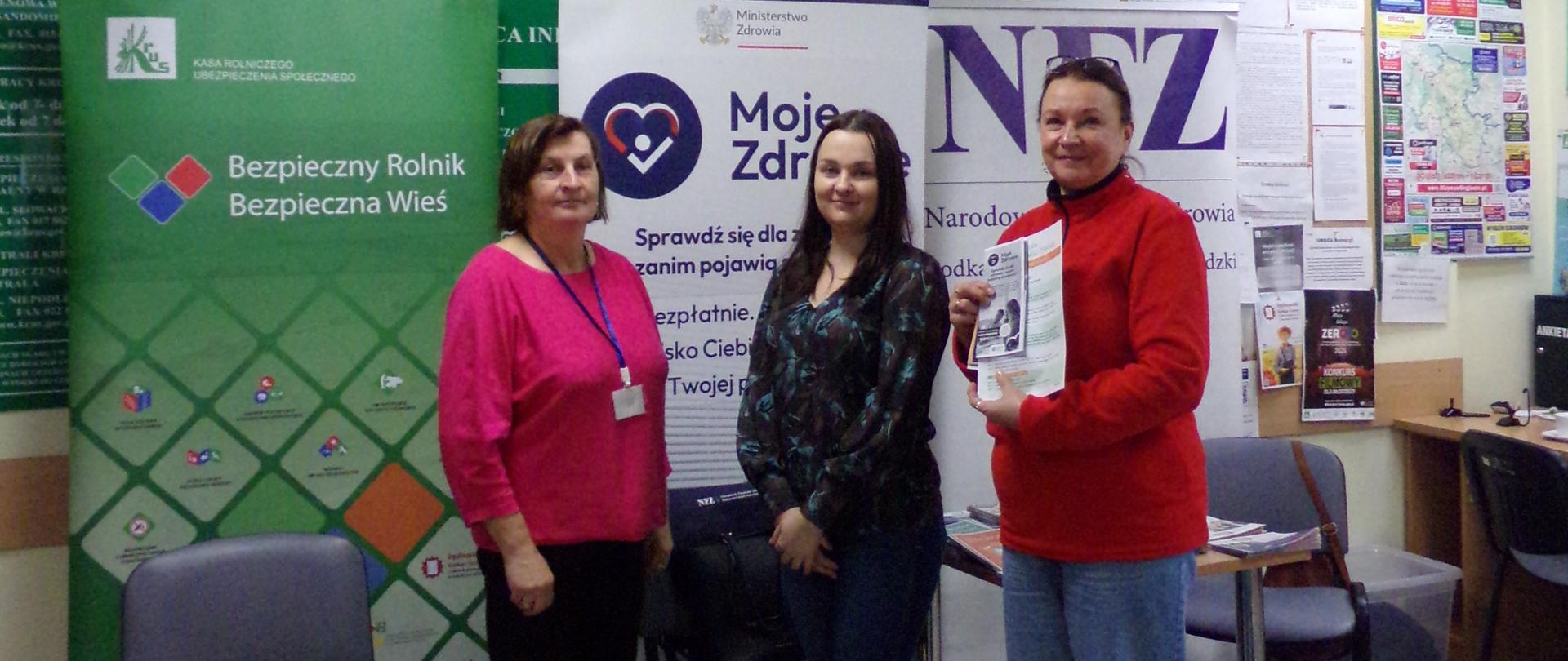 Trzy kobiety pozują do zdjęcia na tle roll-upów KRUS oraz NFZ.