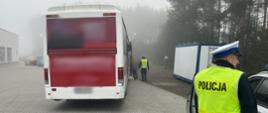 Interwencja funkcjonariuszy Policji na miejscu zatrzymania do kontroli kierowcy autobusu po spożyciu alkoholu. Na pierwszym planie (od prawej): policjant stoi obok oznakowanego radiowozu Policji. W tle: zatrzymany do kontroli drogowej autobus i idący obok niego inspektor ITD i kierowca.