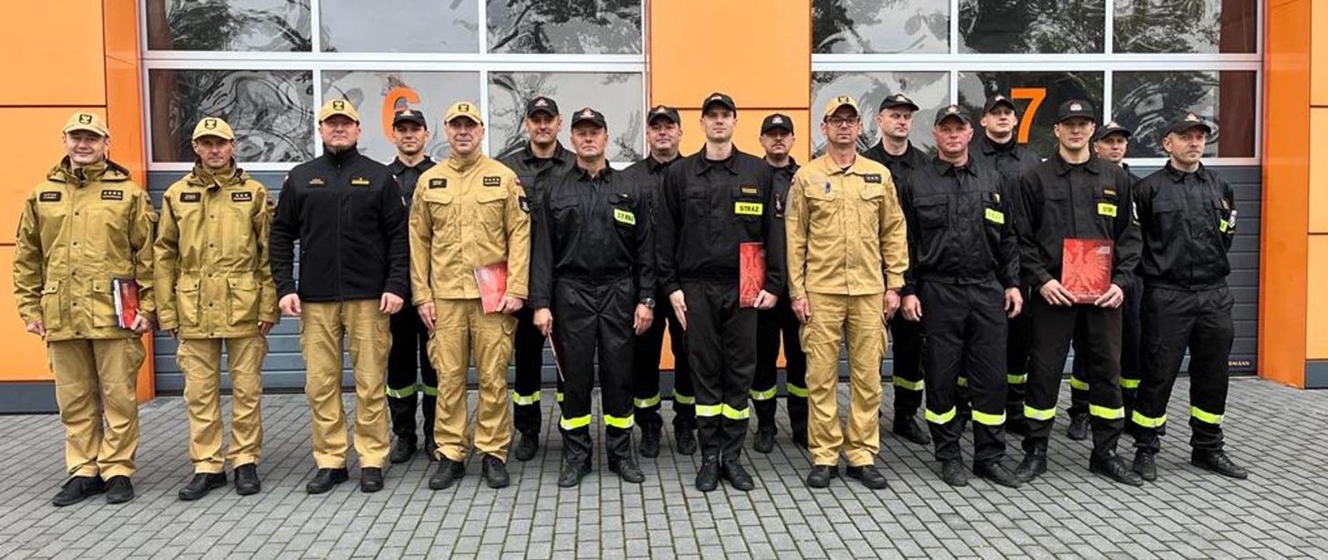 Zdjęcie przedstawia strażaków PSP, którzy są ustawieni przed garażami jednostki w Wolsztynie. 