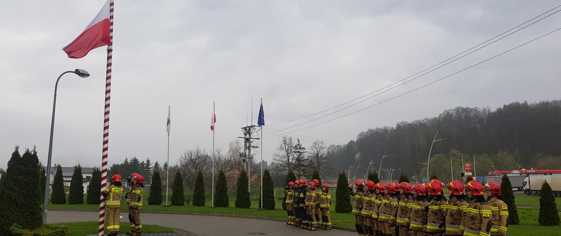 Flaga wciągana jest na maszt a na placu stoją zmiany służbowe.
