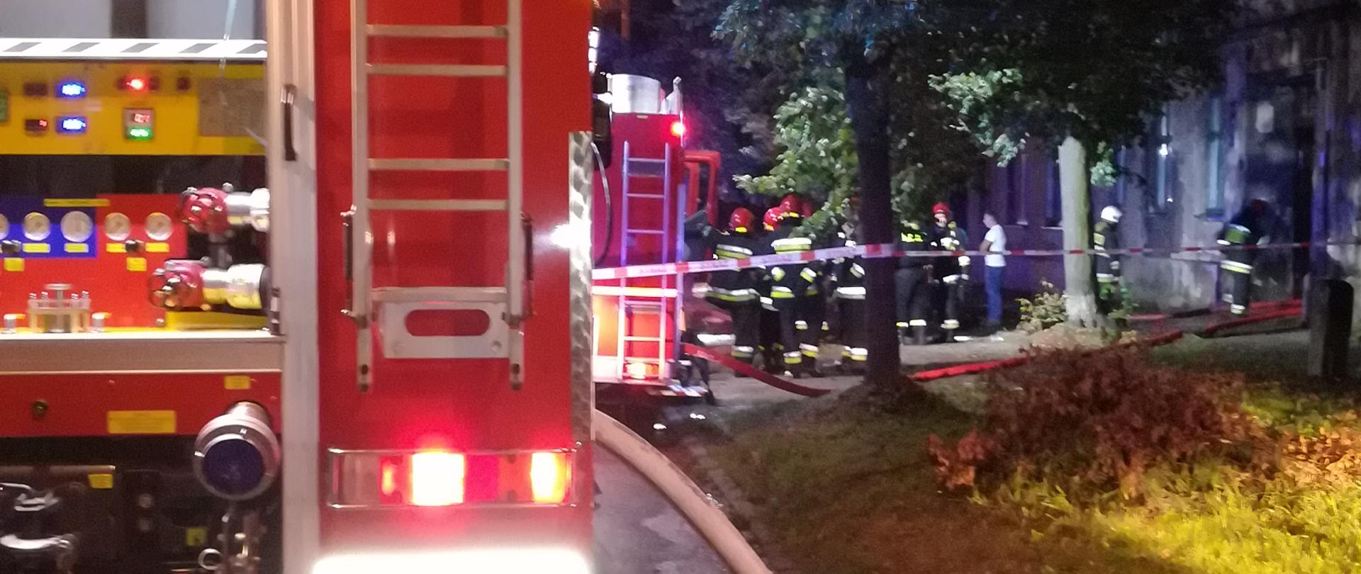 Na zdjęciu samochód pożarniczy w tle pracujący strażacy
