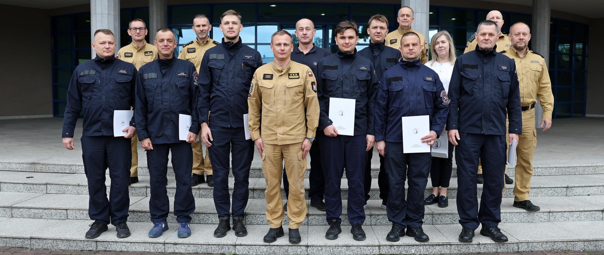 Pamiątkowe zdjęcie grupowe funkcjonariuszy lotniskowej straży pożarnej (8 osób) w towarzystwie Zastępcy Komendanta Centralnej Szkoły PSP, kobiety oraz pięciu funkcjonariuszy CS PSP