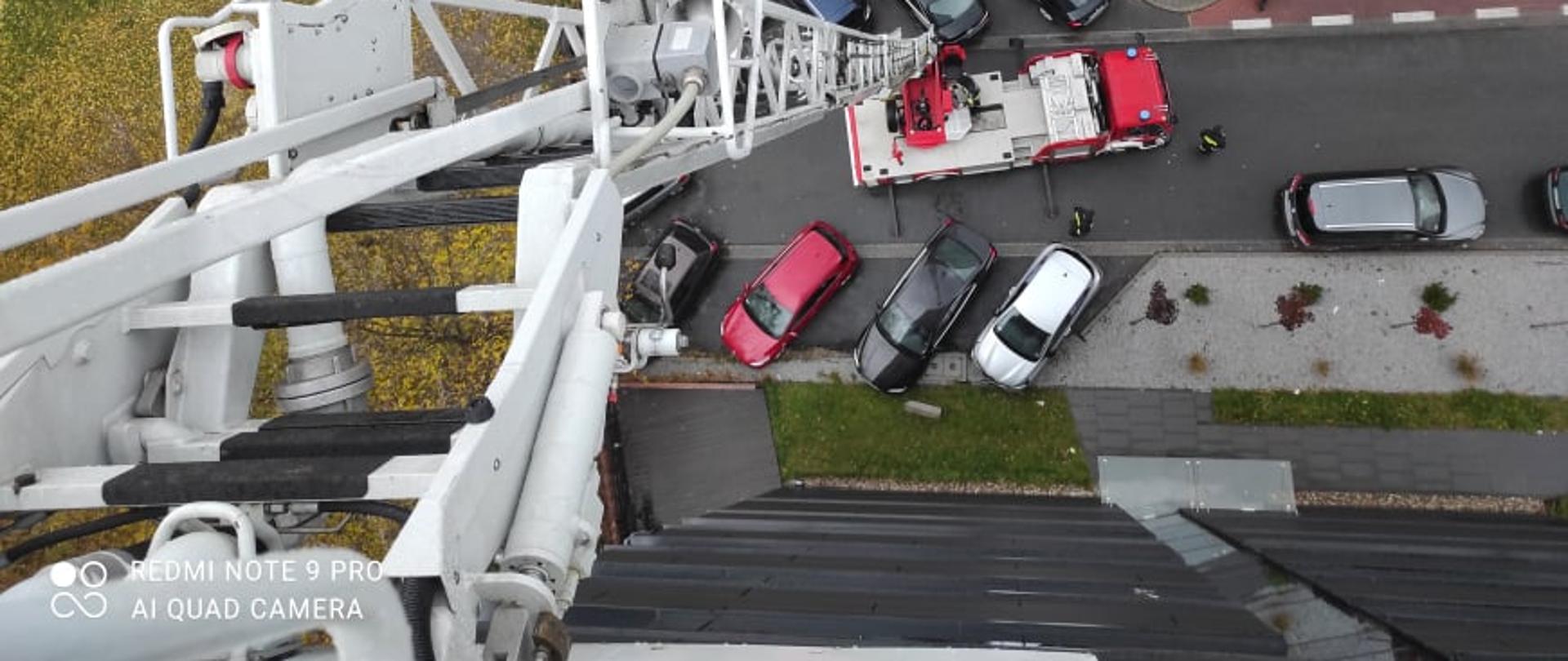 Na zdjęciu widok z kosza drabiny pożarniczej widoczny jest budynek hotelu, trzy samochód straży pożarnej oraz zaparkowane samochody