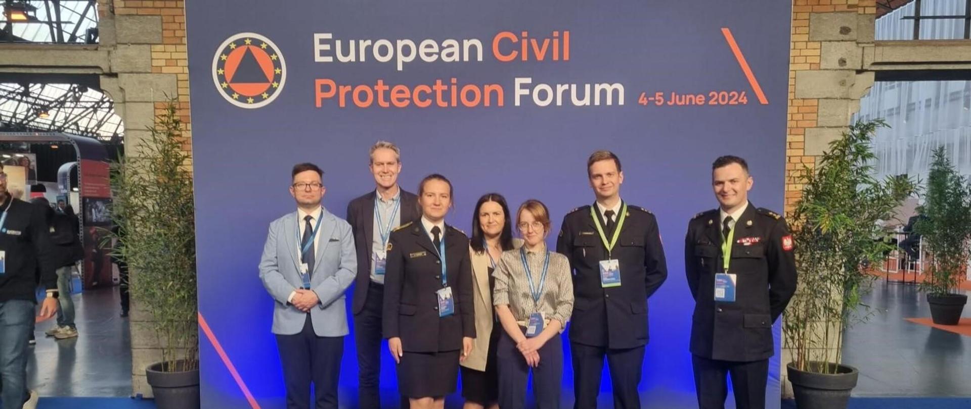 Zdjęcie grupowe strażaków wraz z innymi osobami w tle baner ,,European Civil Protection Forum"