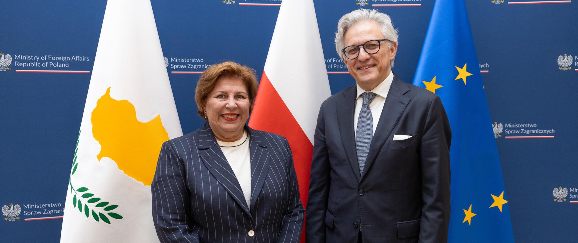 Undersecretary of State Artur Harazim and the Permanent Secretary of the Ministry of Foreign Affairs of the Republic of Cyprus, Theodora Constantinidou, smiling in front of flags and the navy blue backdrop of the Ministry of Foreign Affairs.