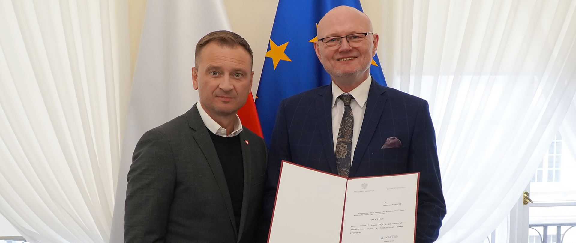 Zdjęcia przedstawia Ministra Sławomira Nitrasa z Ireneuszem Nalazekiem, który został powołany na stanowisko podsekretarza stanu w Ministerstwie Sportu i Turystyki. Panowie stoją na tle flagi Polski i Unii Europejskiej, a Pan podsekretarz trzyma w rękach swoją nominację.