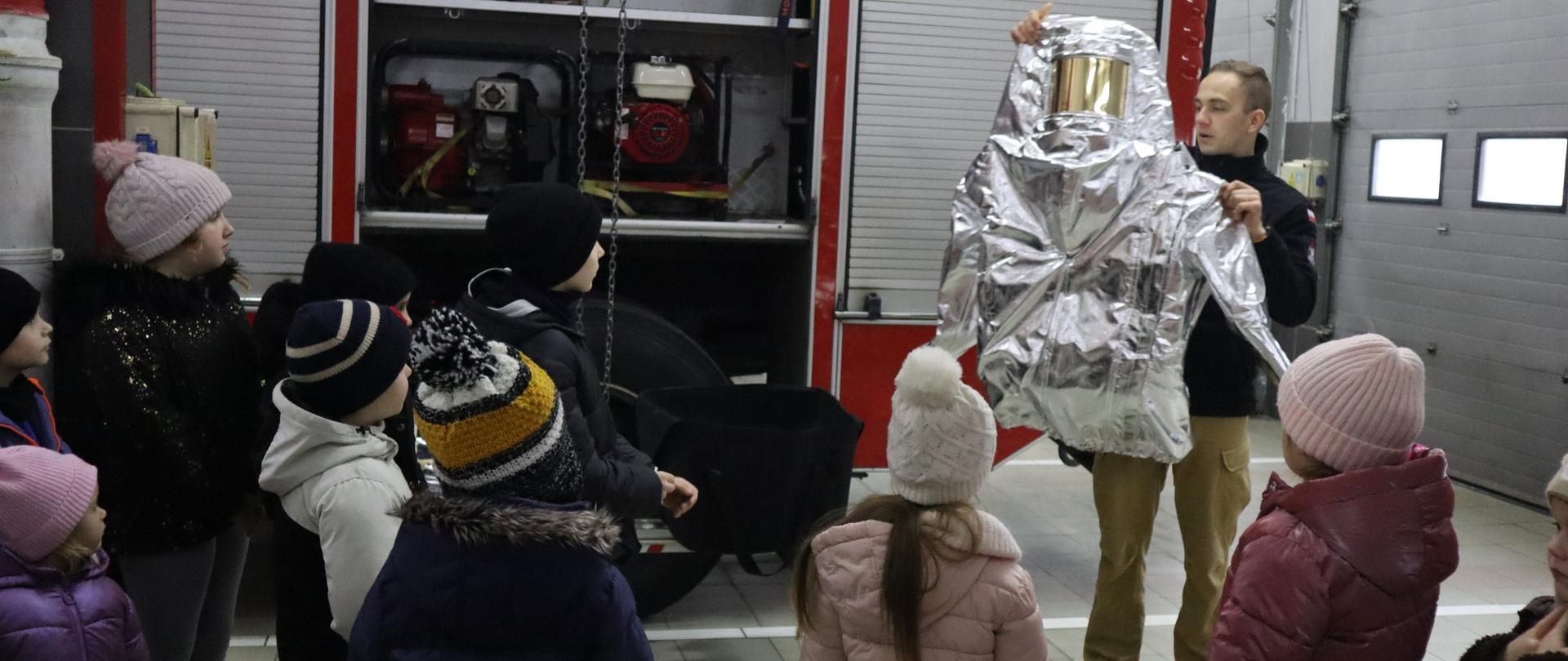 Strażak przedstawiający uczniom ubranie żaroodporne