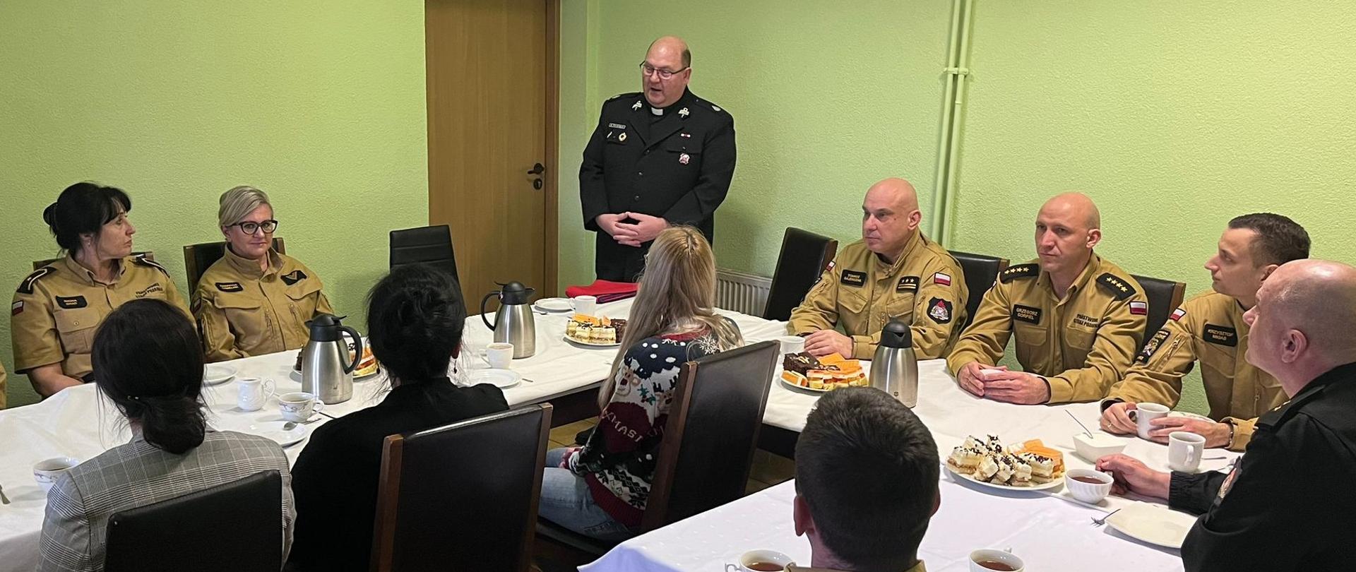 Ksiądz przemawia do zebranych funkcjonariuszy i pracowników cywilnych komendy podczas świątecznego spotkania opłatkowego.