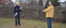 Przygotowywanie spotu edukacyjnego. Jedna z ulic w Dębnie Polskim. Na trawniku stoi policjantka i kamerzysta. Nagrywana jest wypowiedź funkcjonariuszki. W tle płot.
