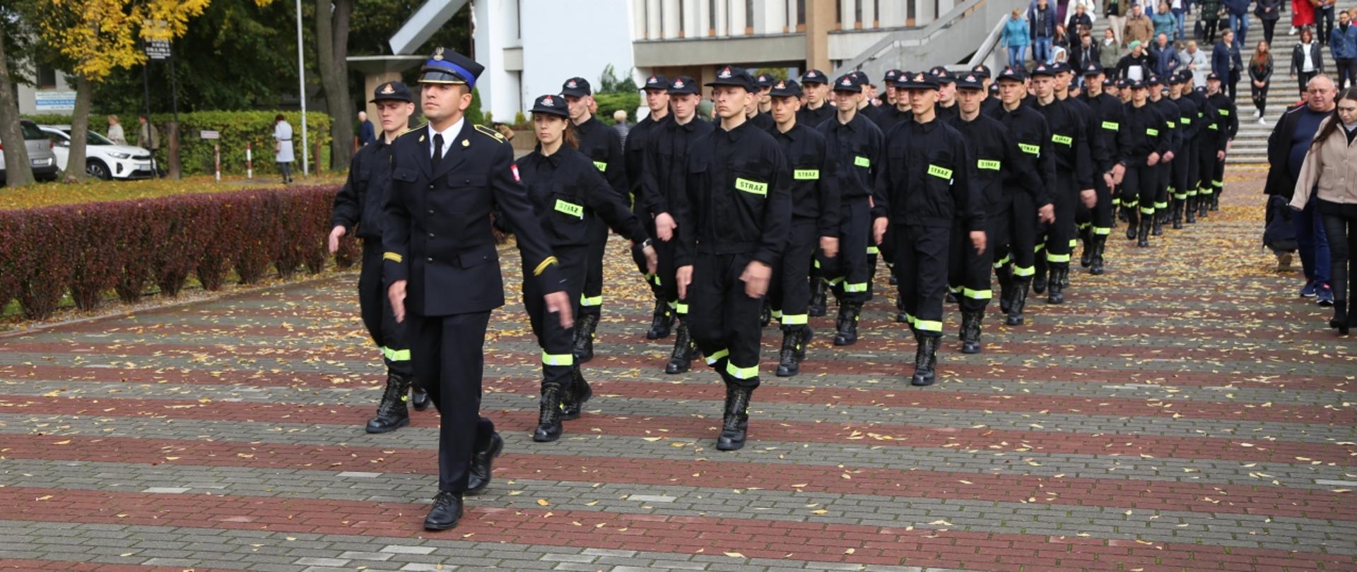 Na zdjęciu maszerująca po wyjściu z kościoła kompania kadetów ustawiona w czterech rzędach. W głębi wierni opuszczający kosciół