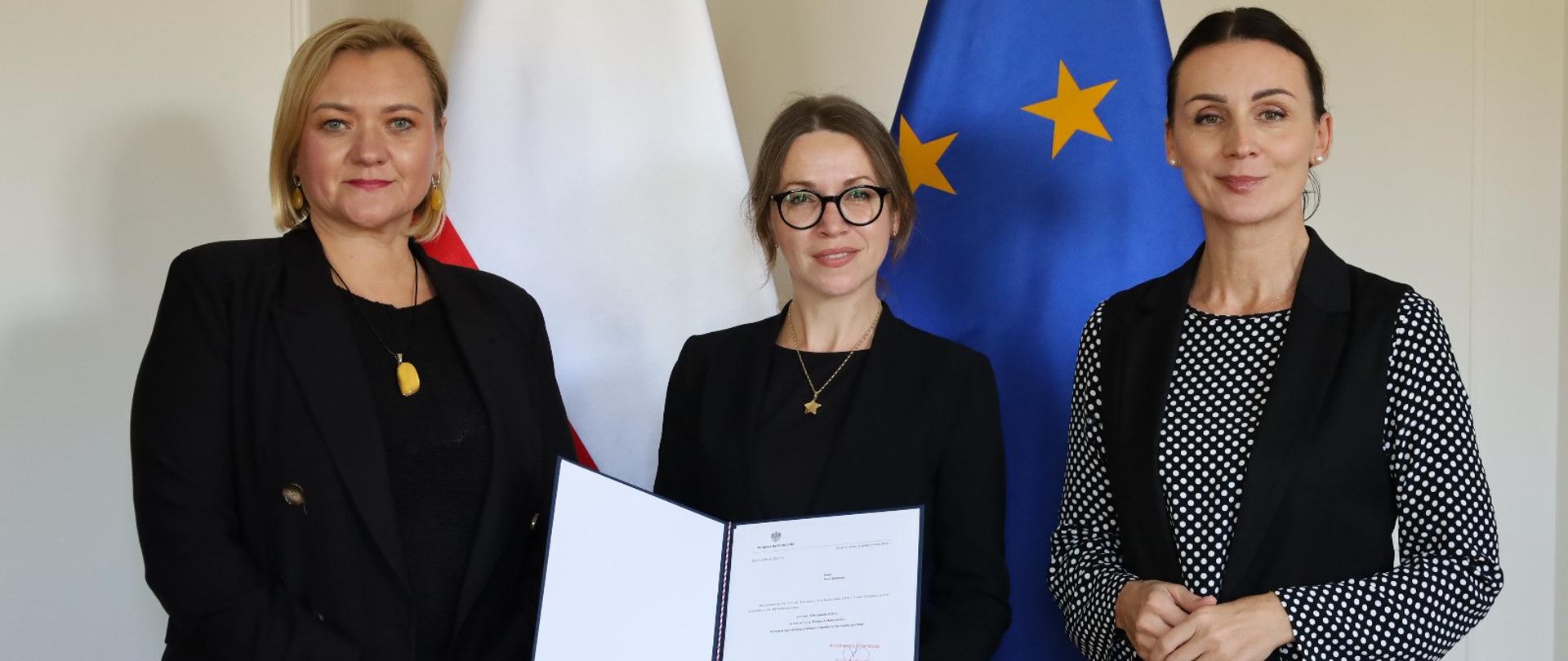 trzy kobiety stoją na tle flagi państwowej