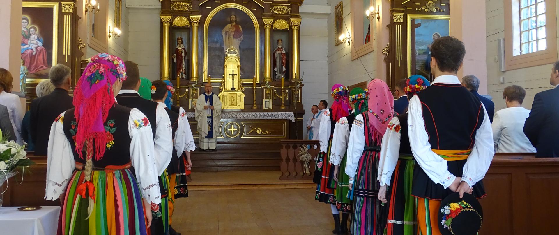 Na zdjęciu widać główny ołtarz w kościele, po lewej i prawej stronie stoją ludzie przy ławkach odwróceni tyłem