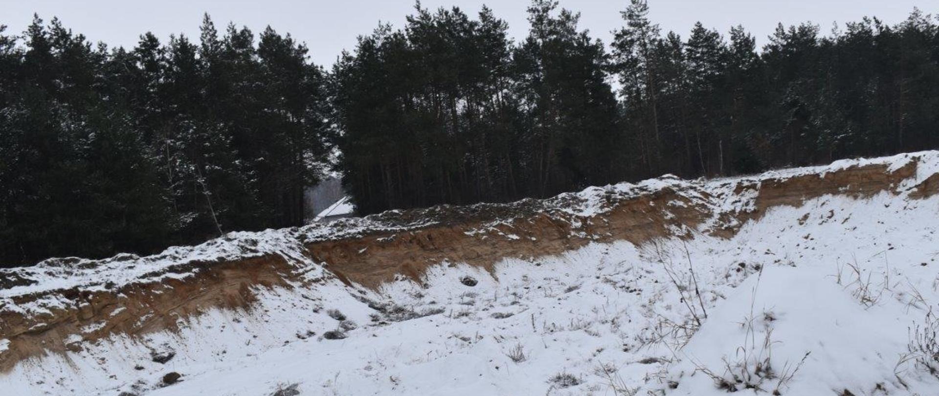Wgłębienie w terenie o powierzchni kilkudziesięciu metrów kwadratowych po wyrobisku żwiru zasypany śniegiem. W tle las.