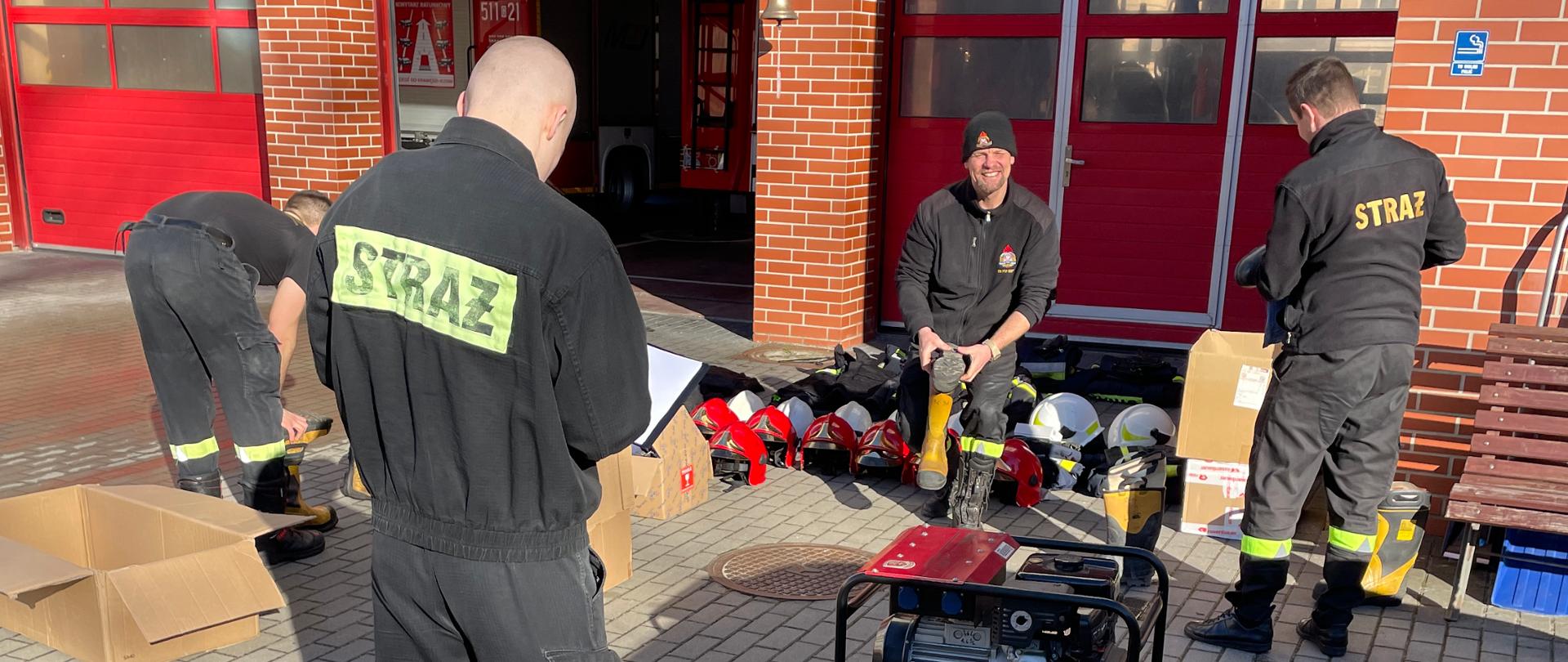 Na placu wewnętrznym strażacy przygotowuja do ułożenia i spakowania sprzęt i wyposażenie takie jak węże srażackie obuwie specjalne czy pompy 