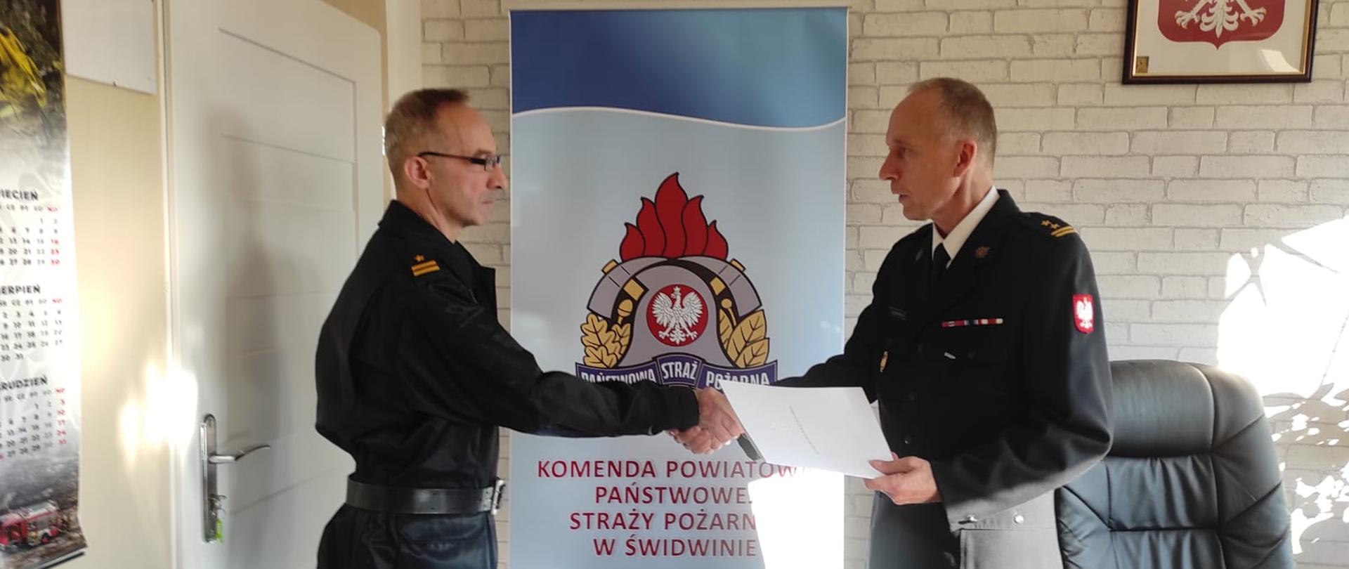 Zdjęcie przedstawia dwóch strażaków podczas wręczania nagrody jubileuszowej.