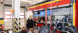 strażak pokazuje wyposażenie samochodu strażackiego na garażu, grupka kilkunastu osób przygląda się otwartej skrytce auta