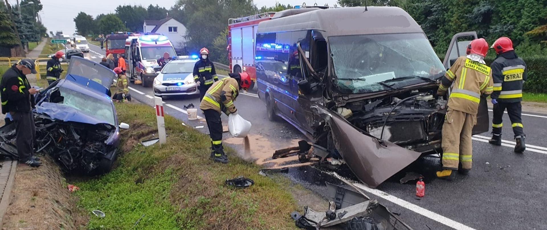 Zdjęcie obrazuje drogę jednopasmową DK 42 na której doszło do zderzenia czołowego samochodu osobowego marki SEAT Leon z Busem Mercedes. W wyniku zdarzenia Bus Mercedes znajdujący się w centralnej części zdjęcia został na jednym pasie ruchu, całkowicie go blokując. Samochód SEAT Leon, który jest z lewej strony zdjęcia znajduje się w przydrożnym rowie. Oba pojazdy mają zniszczony przód. Na zdjęciu strażacy znajdujący się przy busie odłączają akumulator z rozbitego pojazdu oraz posypują wyciekłe płyny eksploatacyjne sorbentem. W tle zdjęcia znajduje się karetka Pogotowia Ratunkowego a za nią samochody pożarnicze.