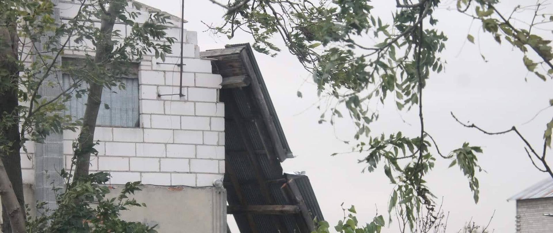 Fragment uszkodzonego dachu oparty o budynek mieszkalny. Dach został zerwany przez wiatr. Strażacy podejmują działania celem zabezpieczenia obiektu