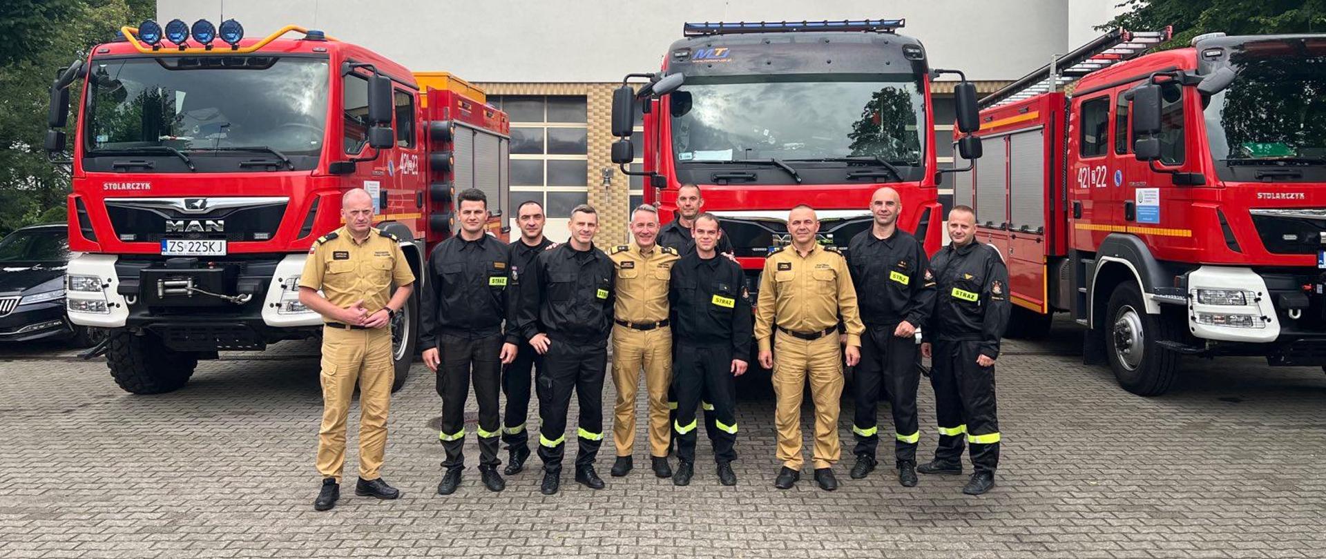 wspólne zdjęcie strażaków przed samochodami na tle budynku 