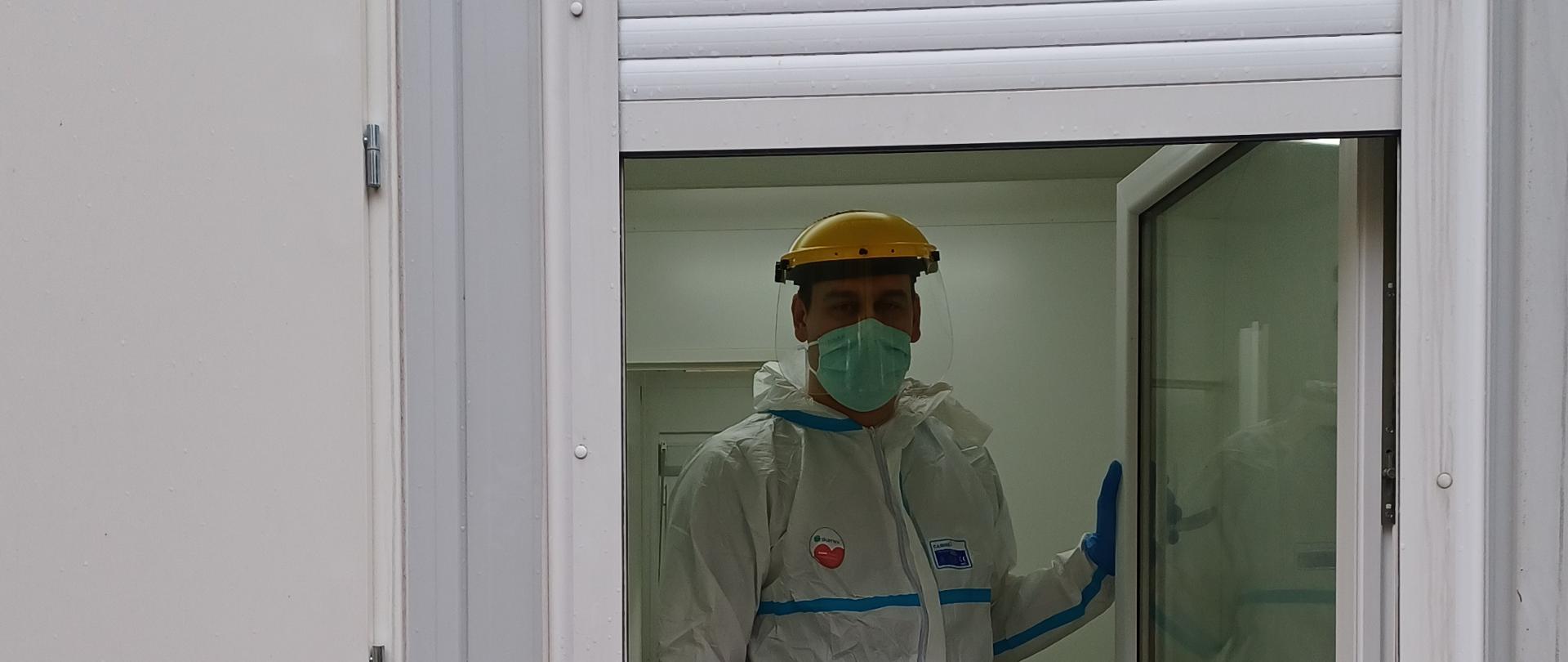 Strażak zabezpieczony w ubraniu stoi wygląda przez okno z punktu wymazowego