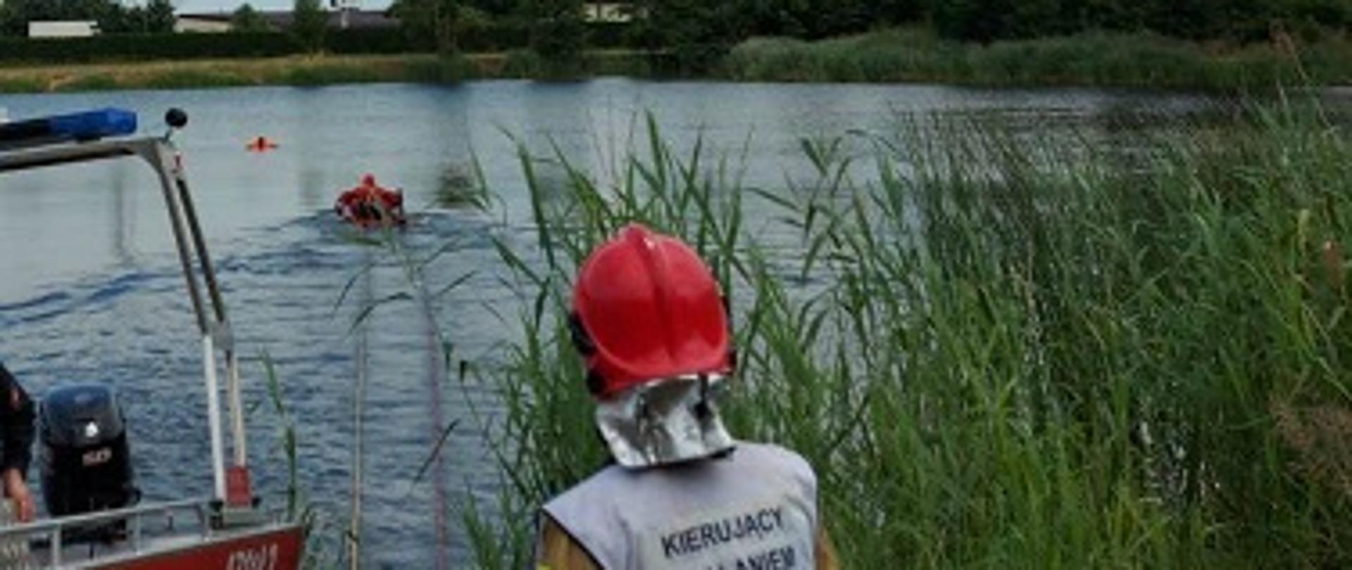 Zdjęcie przedstawia kierującego działaniami ratowniczymi oraz strażaka płynącego do osoby poszkodowanej na saniach lodowych