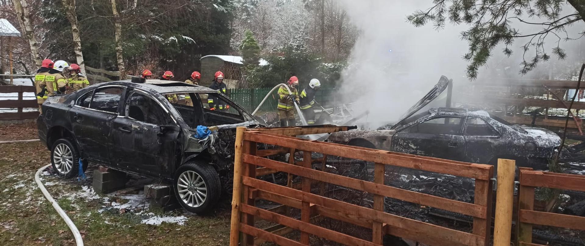Zdjęcie przedstawia trwającą akcję gaśniczą na działce rekreacyjnej w Kuligowie nad jeziorem Żółwin. Doszczętnie zniszczone przyczepy campingowe oraz częściowo spalone 2 pojazdy osobowe znajdujące się w bezpośrednim sąsiedztwie przyczep.