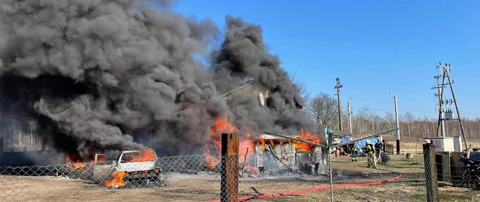 Widać pożar budynku i samochodu osobowego, jest czarny dym