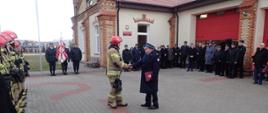 Komendant powiatowy PSP w Grajewie wręcza nagrodę funkcjonariuszowi PSP na placu przed budynkiem Komendy Powiatowej PSP W Grajewie.