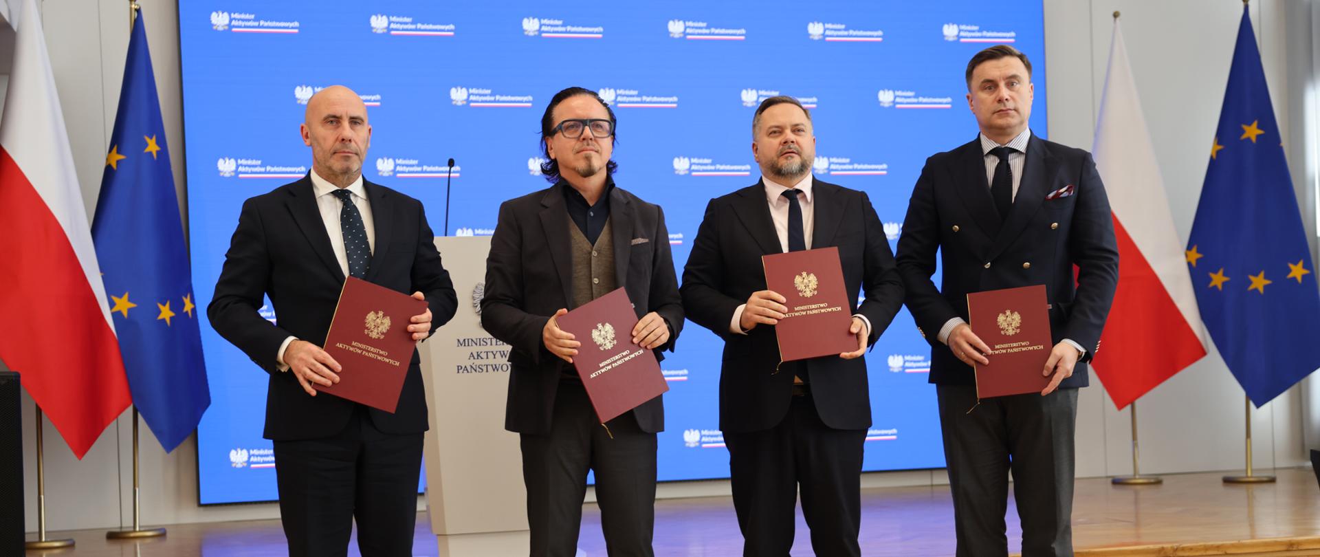 Od lewej: prezes Zarządu PGZ Adam Leszkiewicz, minister Wojciech Balczun, wiceminister Konrad Gołota i wiceprezes Zarządu PGZ Marcin Idzik na tle ścianki z logotypami MAP i mównicy.