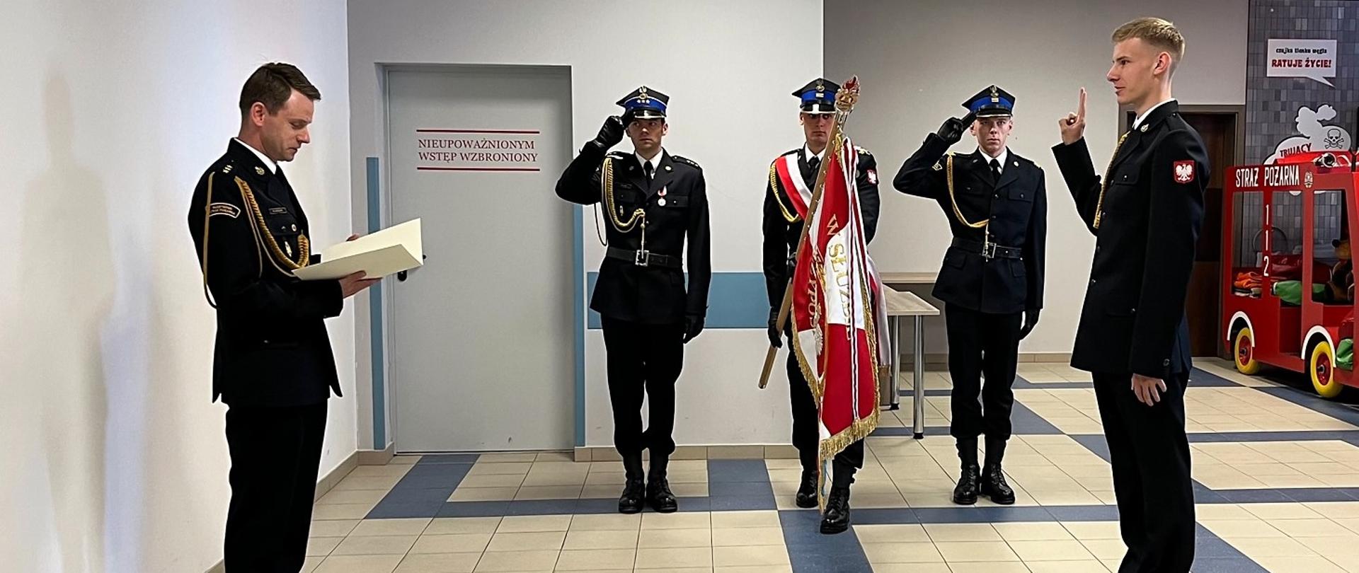 Ślubowanie strażaka Doriana Mielewczyka złożone przed komendantem powiatowym PSP w Wąbrzeźnie kpt. Robertem Stasiakiem. W tle poczet sztandarowy.