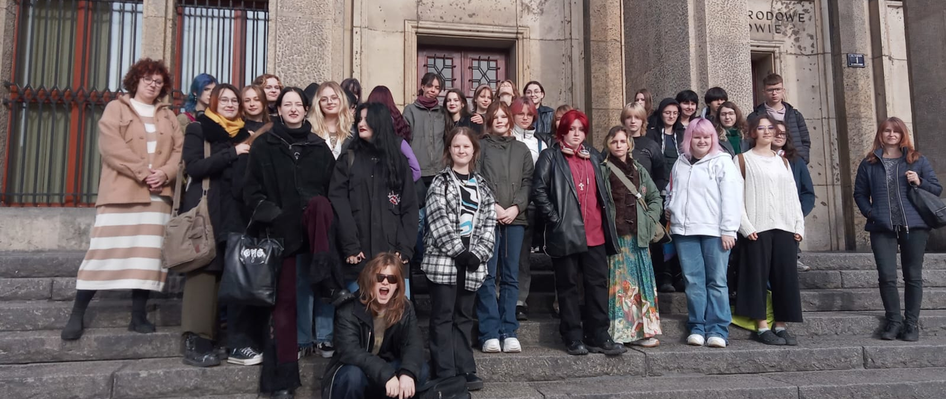 Grupa uczniów i nauczycieli na schodach Muzeum Narodowego w Krakowie.