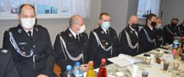 Zjazd OP ZOSP RP w Rawiczu. Sala wiejska w Rogożewie. Za stołem zasiadają uczestnicy Zjazdu - strażacy w mundurach wyjściowych.Na twarzach mają maseczki ochronne. Na stole znajdują się kubki i napoje.
