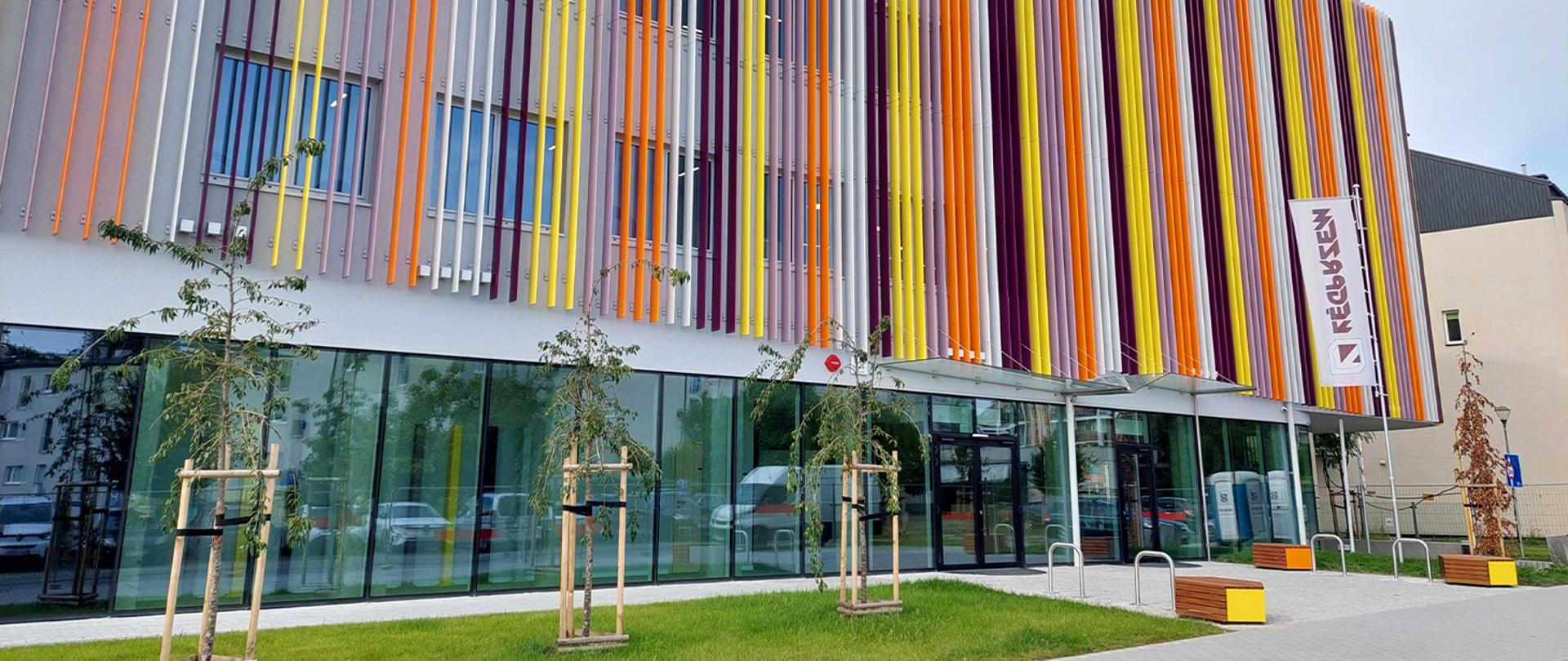 Fasada Centrum Kultury Ruczaj w Krakowie, widok na główne wejście i wielobarwne pionowe panele elewacyjne.