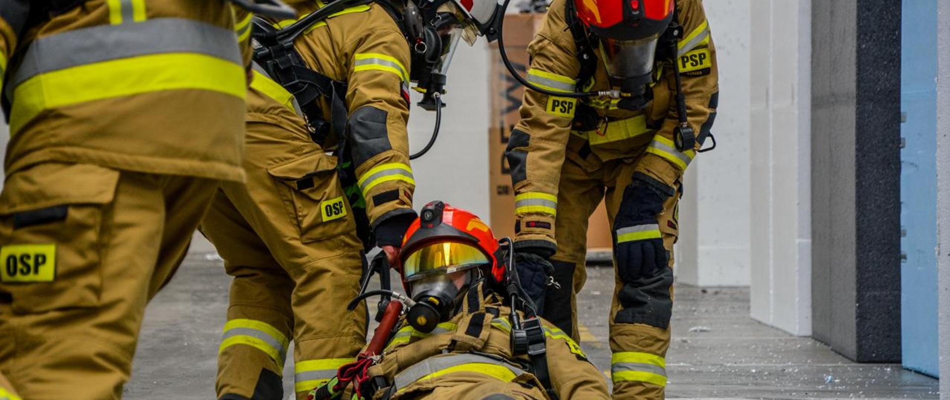 Strażacy w pełnym umundurowaniu w trakcie ćwiczeń ratowniczych w hali zakładu Styropian Plus.