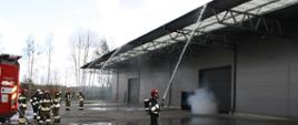 Strażacy podają prądy wody na dach hali w aparatach ochrony dróg oddechowych