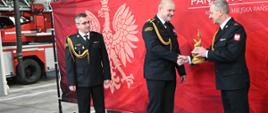 Komendant wręcza strażakowi pamiątkową statuetkę. 
