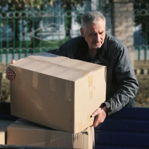 Starszy mężczyzna podnosi jedno z pudeł z pomocą materialną