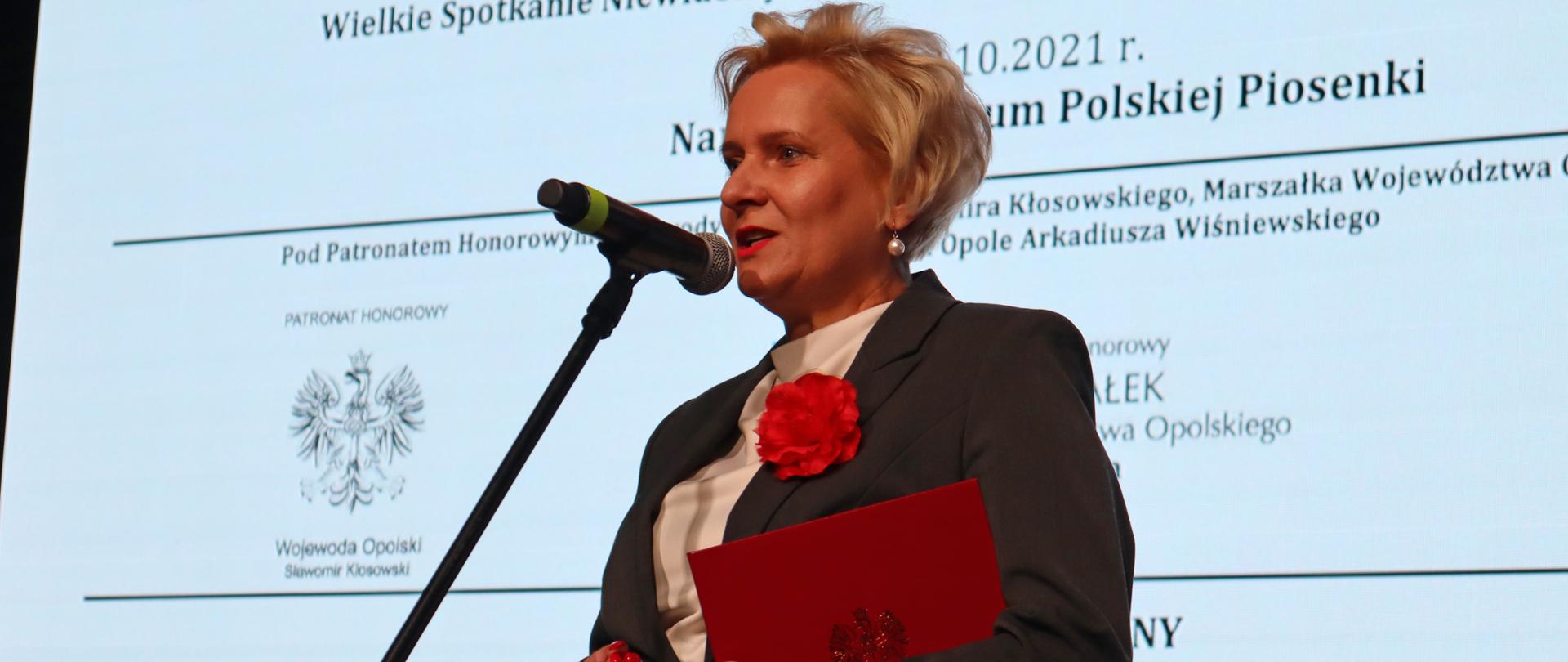 na zdjęciu Wicewojewoda opolski na konferencji REHA 2021. Przemawia za mikrofonem. W tle monitor. 