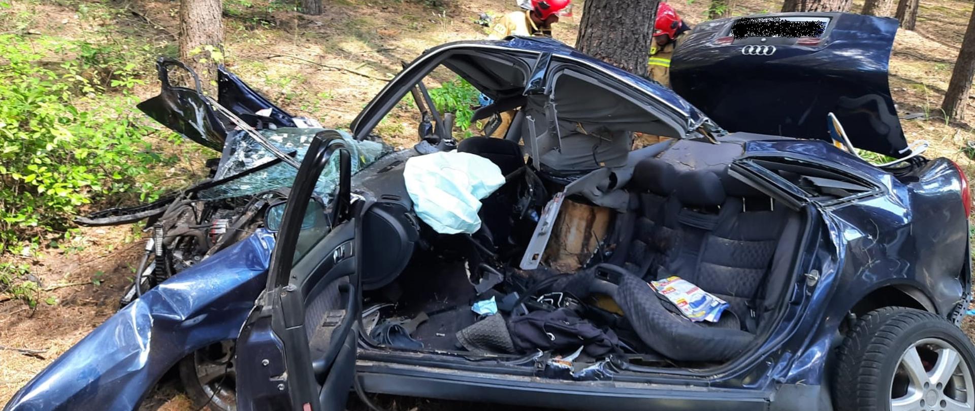 Widać uszkodzony samochód od strony kierowcy, który bokiem od strony pasażera uderzył w drzewo