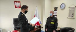 Na zdjęciu Komendant Powiatowy PSP w Myśliborzu wręczający strażakowi gratulacje. Obaj znajdują się w gabinecie. Na ścianie wisi godło Rzeczypospolitej Polskiej.