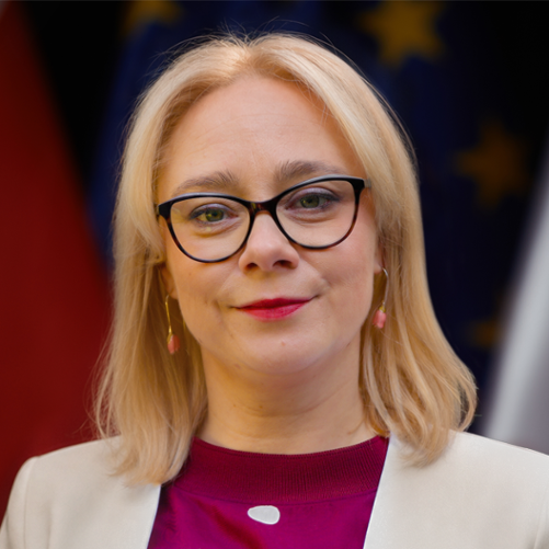 Wiceminister sportu i turystyki Żaneta Cwalina-Śliwowska na tle flag Polski i UE.