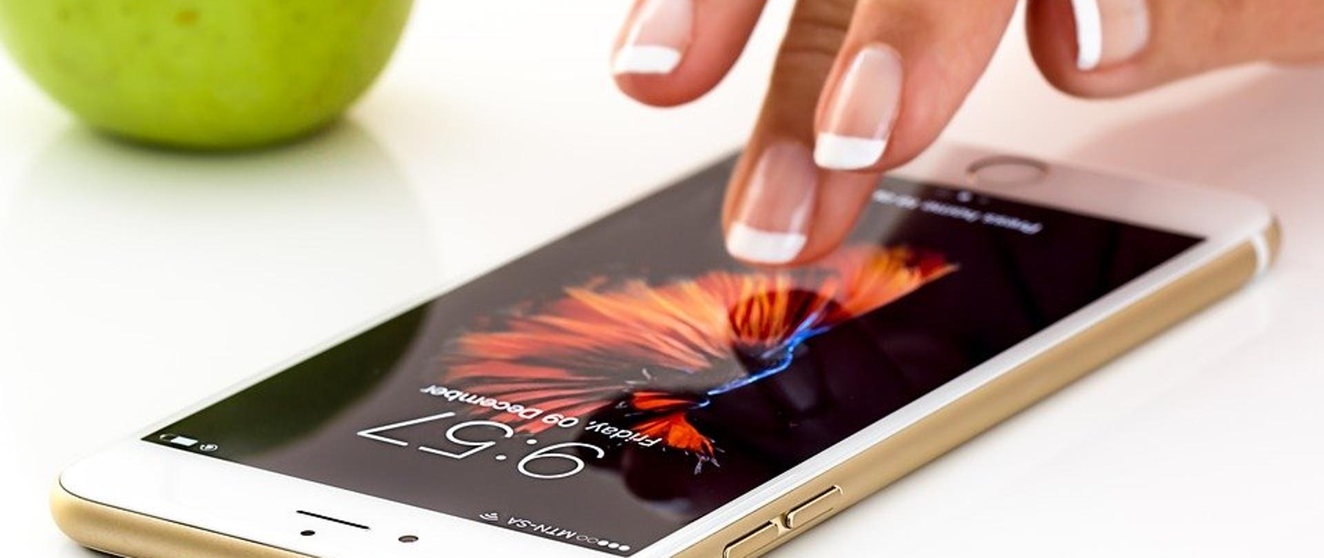 Zdjęcie w poziomie. Kobieca dłoń dotykająca telefonu.