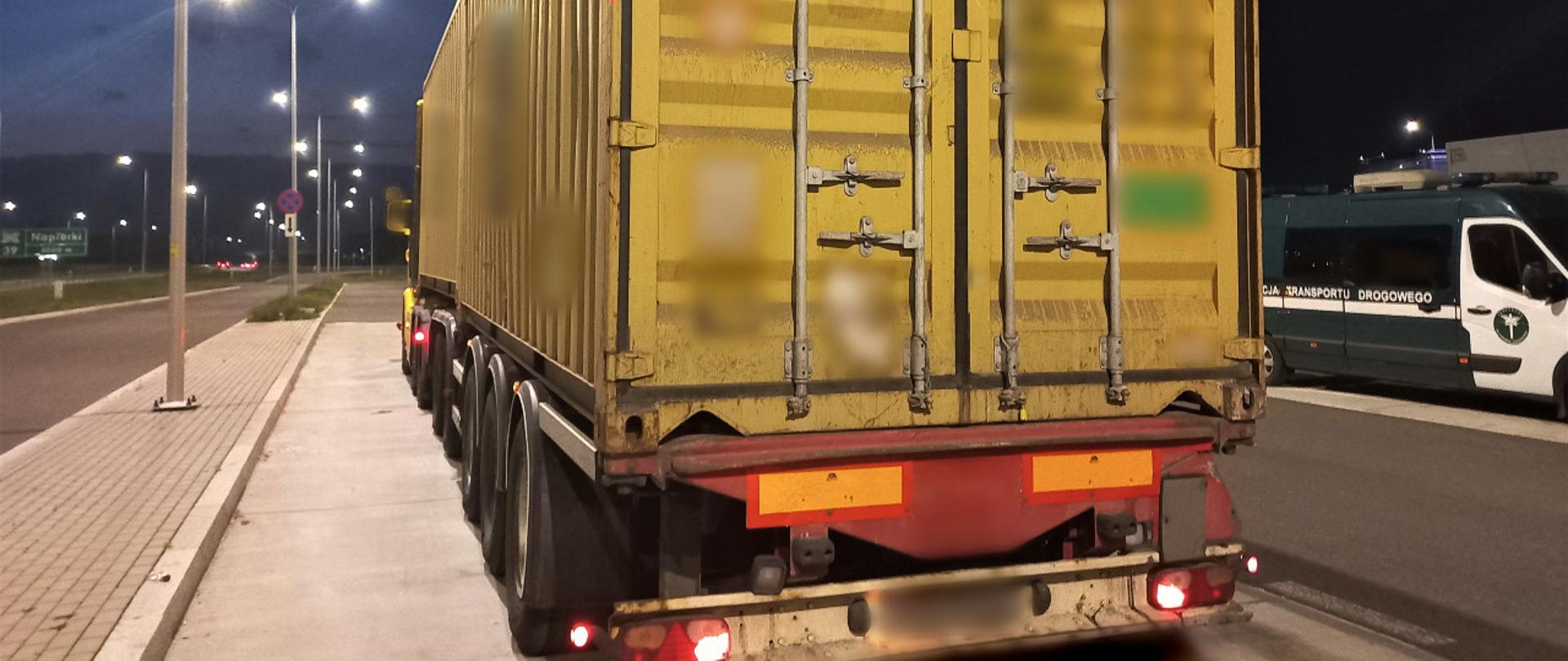 Na pierwszym planie: w zatoce kontrolnej stoi ciągnik siodłowy z podpiętą naczepą dzieloną. Zestaw przewozi ładunek w dwóch kontenerach 20-stopowych. W tle: obok kontrolowanego zestawu ciężarowego, po prawej stronie, stoi oznakowany furgon mazowieckiej Inspekcji Transportu Drogowego. 