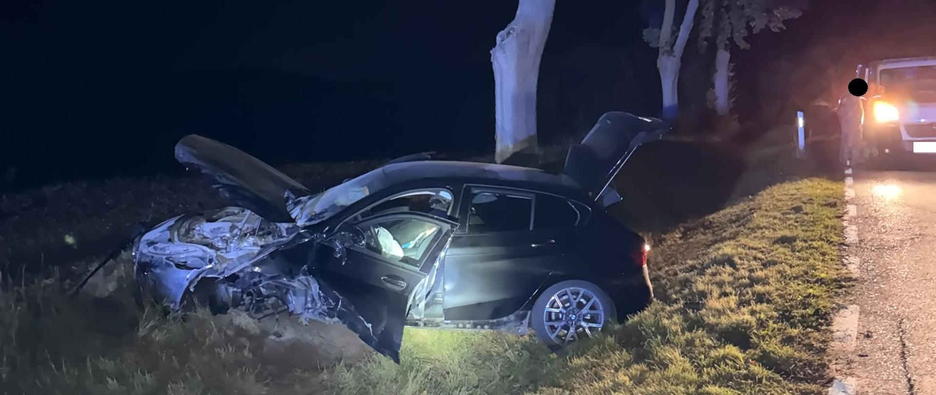 Czarny uszkodzony samochód w rowie, jest ciemno