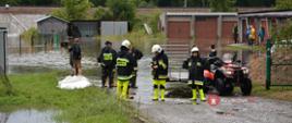 Grupa strażaków stoi nad rozlewiskiem, zalane garaże