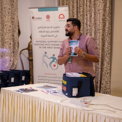 Obok stołu stoi mężczyzna i prezentuje zawartość torby z zestawem sensorycznym