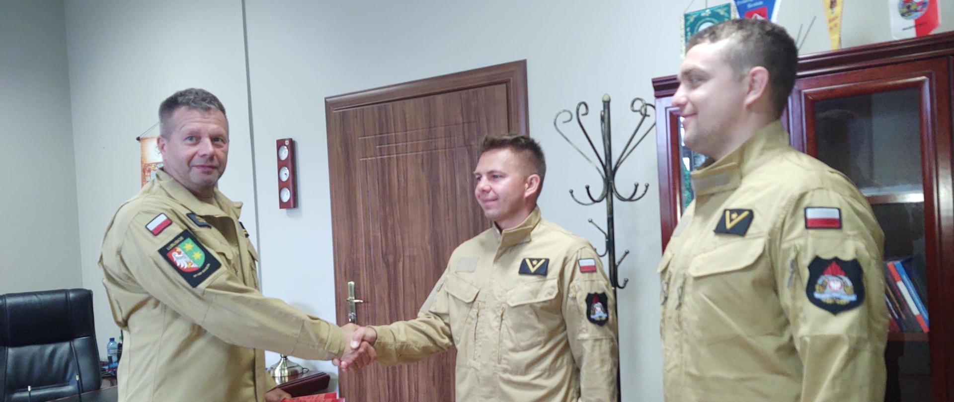 Komendant Powiatowy ściska dłoń wyróżnionego strażaka obok stoi drugi strażak