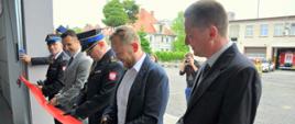 Zdjęcie przedstawia moment przecięcia wstęgi podczas otwarcia obiektu biurowo-garażowego w Komendzie Powiatowej Państwowej Straży Pożarnej w Lwówku Śląskim.