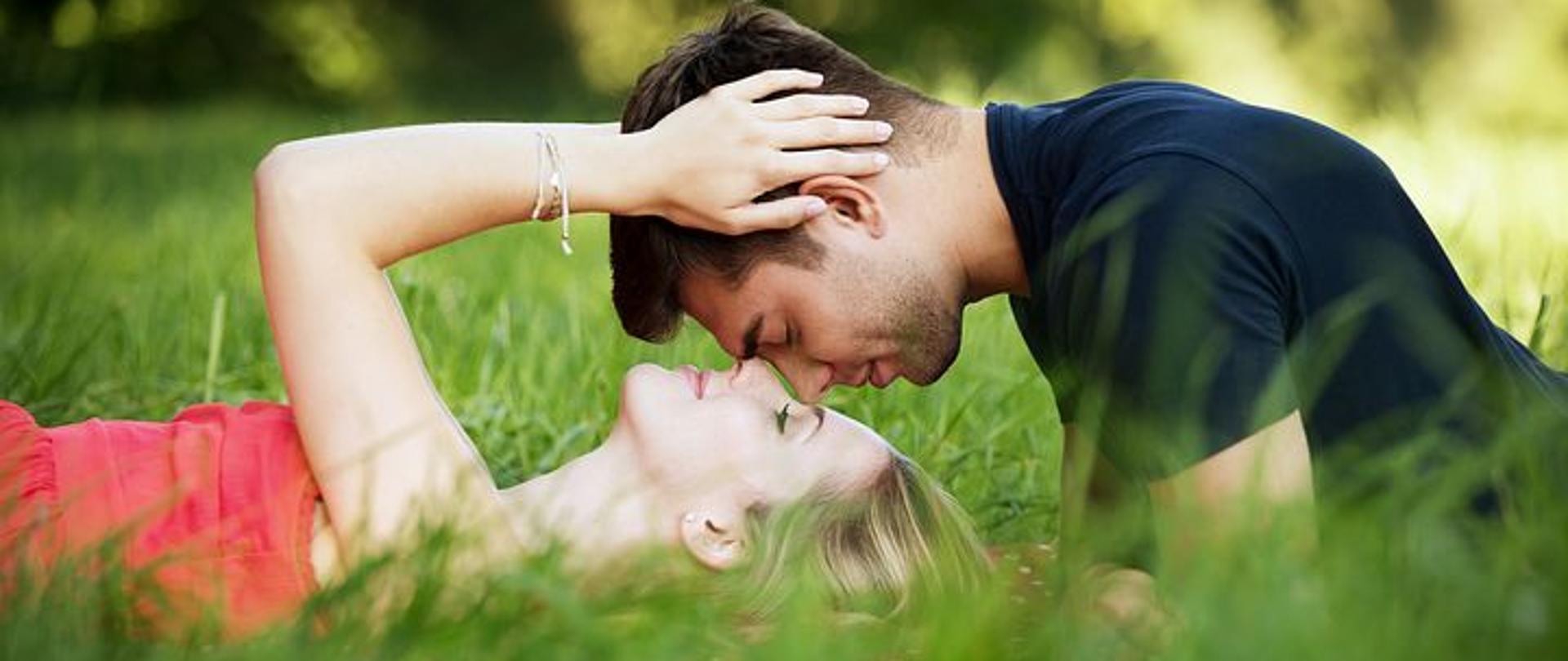 mężczyzna dotyka nosem kobietę i leżą na zielonej łące